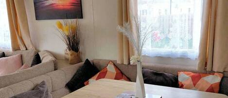 Una sala de estar con un sofá, una mesa con un florero y libros, y un cuadro en la pared.