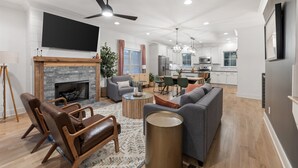 A modern living room with a fireplace, leather chairs, a gray sofa, and a dining area with a chandelier. - Rooftop Relaxation in Downtown Murfreesboro (Murfreesboro)