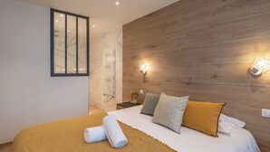 Un dormitorio moderno con cabecera de madera, una cama grande con ropa blanca y una pared divisoria de vidrio.