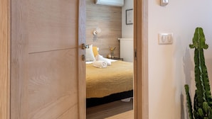 Un dormitorio con un armario de madera, una cama con una manta amarilla, una mesita de noche con una lámpara y una planta de cactus.