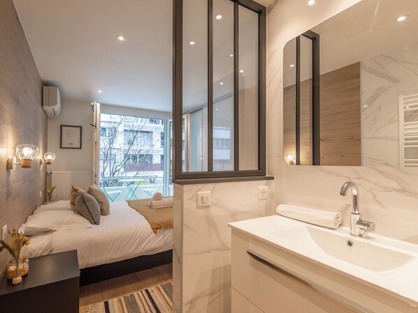 A modern bedroom with a large bed, bedside table with a vase, and a view of the outside.