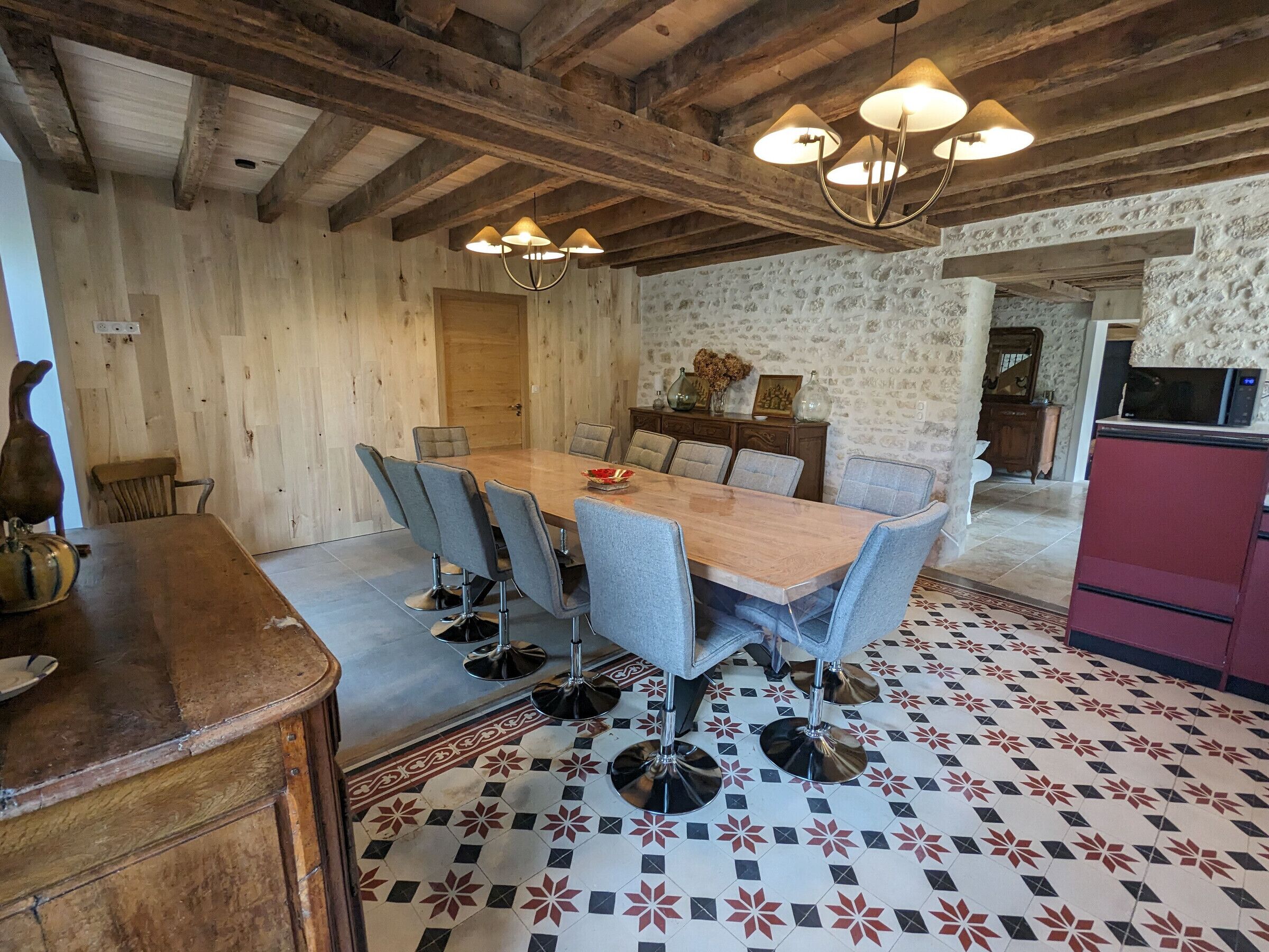 A dining area with a wooden table and grey upholstered chairs, a decorative vase, and a patterned floor.