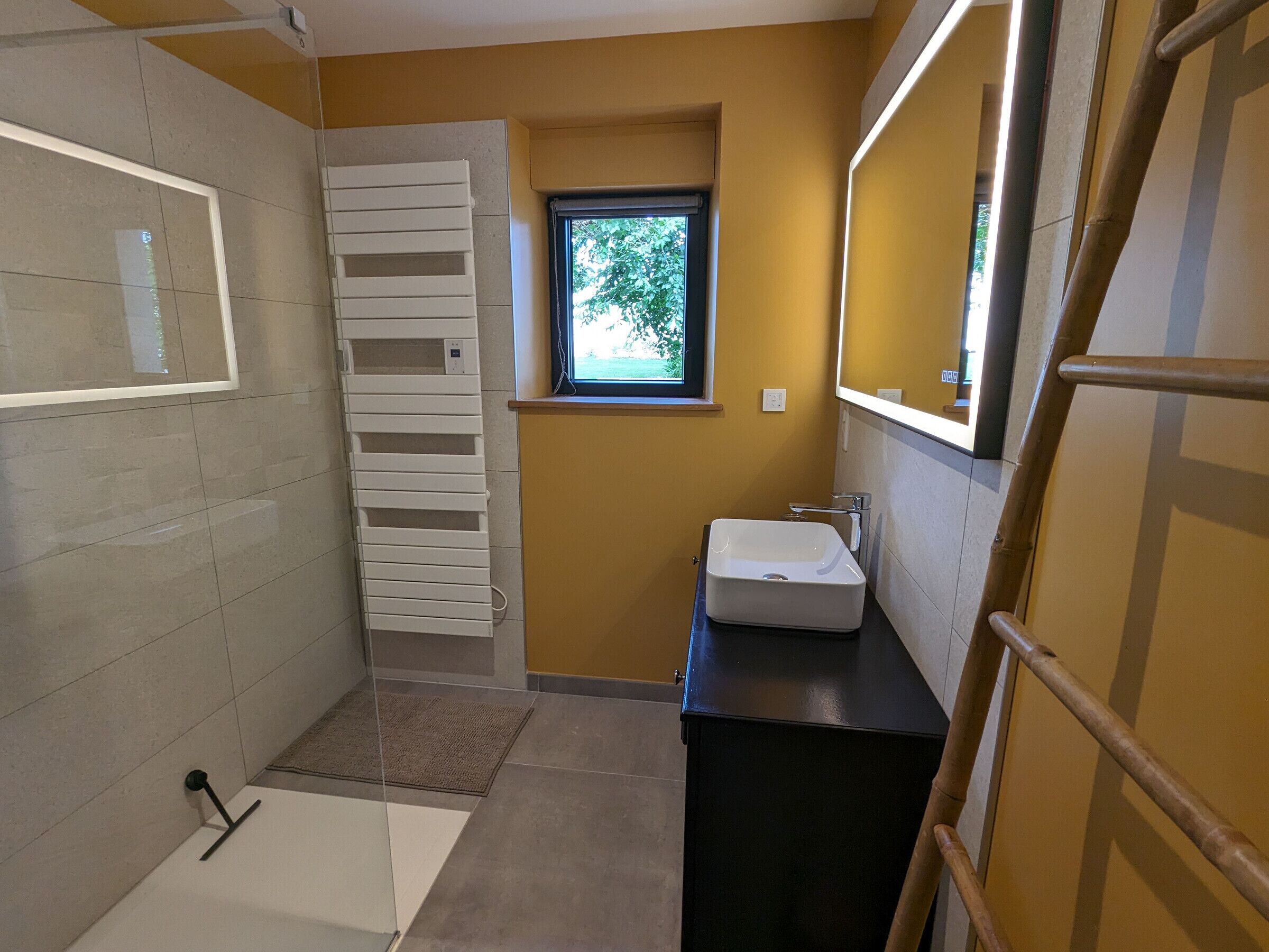 Ein kleines Badezimmer mit einer weißen Badewanne, einem weißen Waschbecken, einem Fenster und einer Holzleiter.