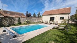 A swimming pool with lounge chairs, a stone wall, and a building with a tiled roof. - Family-Friendly Getaway: Heated Pool, Garden, Near Fontainebleau & Paris (Aulnay-la-Rivière)