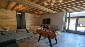 A spacious living room with a sofa, a foosball table, and a television. - Family-Friendly Getaway: Heated Pool, Garden, Near Fontainebleau & Paris (Aulnay-la-Rivière)