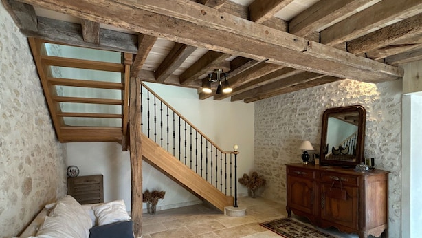 A rustic interior with exposed wooden beams, a staircase, a wooden dresser, and a stone wall. - Family-Friendly Getaway: Heated Pool, Garden, Near Fontainebleau & Paris (Aulnay-la-Rivière)