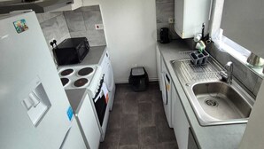 A compact kitchen with a refrigerator, stove, microwave, sink, and a clock on the wall.