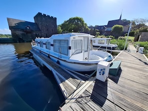 Un bateau était amarré à un quai en bois, avec un chùteau en arriÚre-plan.