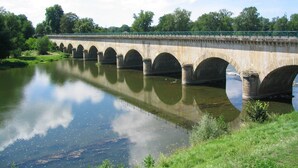 A stone bridge with multiple arches spanning a calm river, surrounded by greenery and a clear sky. - Unique Stay on a Boat in Digoin (Digoin)