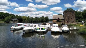 A river with several boats docked near a historic stone building. - Journey on Iris - Houseboat for 5 guests (Chenillé-Changé)