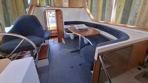 A compact interior with a seating area, a small table, and a window. - Journey on Iris - Houseboat for 5 guests (Chenillé-Changé)