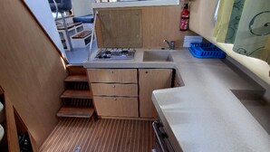 A compact kitchenette with a stove, sink, and wooden cabinets. - Journey on Iris - Houseboat for 5 guests (Chenillé-Changé)