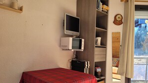 Une petite pièce comprenant un lit, une télévision, un four à micro-ondes et une fenêtre avec des rideaux.
