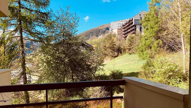 Un balcon donnant sur une colline, des arbres et un bâtiment en arrière-plan.