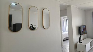 Een hotelkamer met drie spiegels aan de muur, een witte tv-meubel en een bed op de achtergrond.