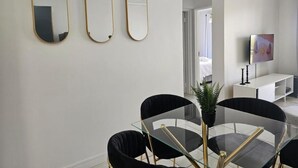 Een moderne kamer met een glazen eettafel, zwarte stoelen en drie spiegelbeelden met gouden lijst.