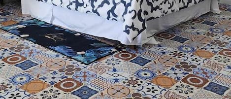 Une chambre à coucher avec une couvre-lit à motifs, une fenêtre à cadre bleu et un sol carrelé présentant différents motifs.
