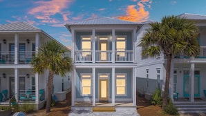 A two-story beachfront property with a balcony, palm trees, and a beachside view.
