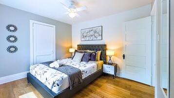 Une chambre à coucher avec un lit, des tables de chevet, un ventilateur de plafond et une porte.