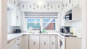 A kitchen with white cabinets, a built-in microwave, a stove, and a window with a view of a brick building.