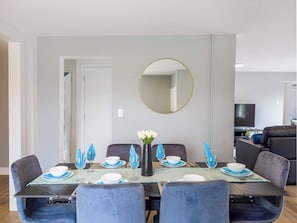 Un coin repas agrémenté d’un miroir rond, d’un téléviseur et d’un canapé en arrière-plan.