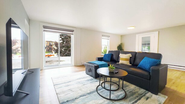 A modern living room with a sofa, a coffee table, a TV, and a sliding glass door leading to an outdoor area.