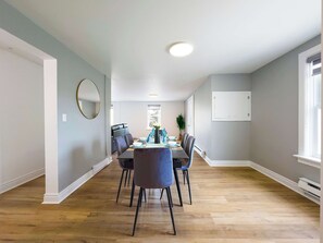 A dining area with a table set for six, surrounded by chairs, a potted plant, and a large mirror on the wall.