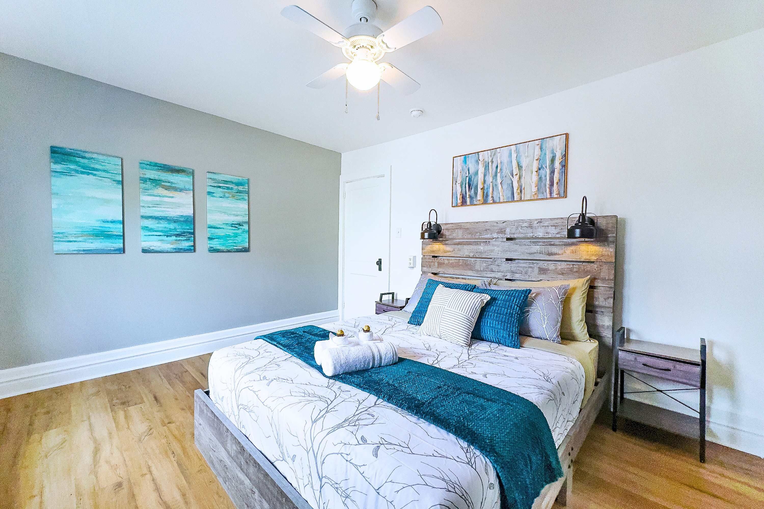 Un dormitorio con cama, ventilador de techo, obras de arte en la pared y cabecero de madera.