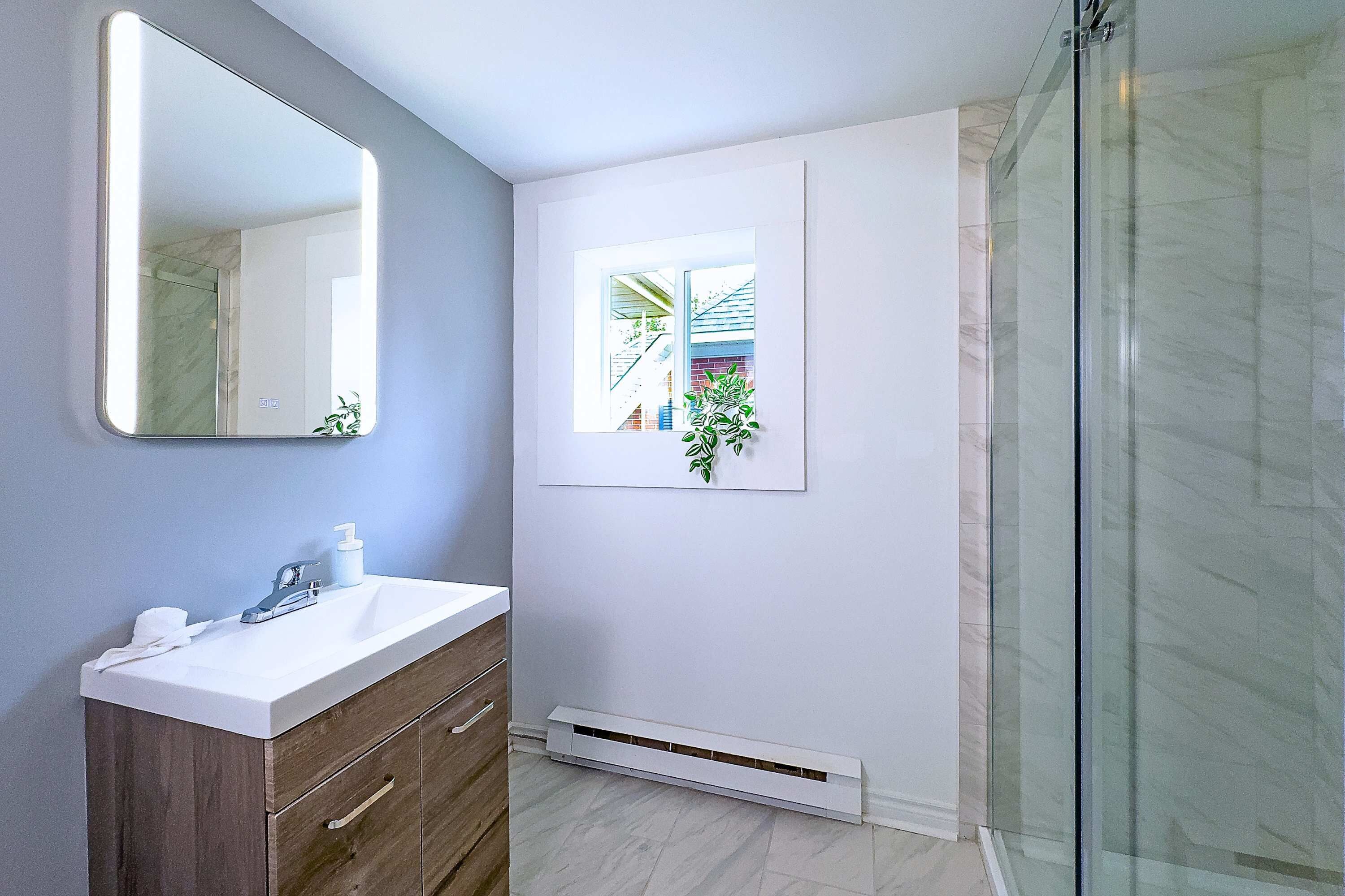 A bathroom with a white vanity, a mirror, a framed picture on the wall, and a glass shower enclosure.