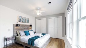 A bedroom with a bed, a ceiling fan, a painting, a wardrobe, and a window.