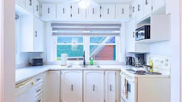 Une cuisine avec des meubles blancs, un four à micro-ondes encastré, une cuisinière et une fenêtre donnant sur un immeuble en briques.