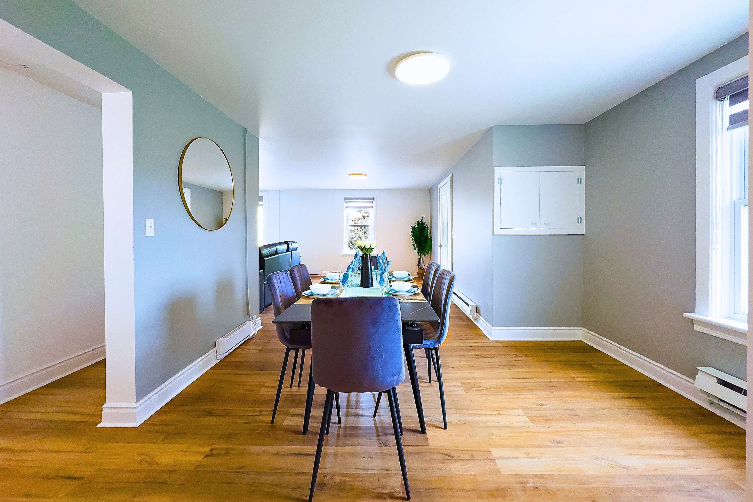 Un coin repas avec une table dressée pour quatre personnes, entourée de chaises, dans une pièce au plancher en bois et aux murs de couleur claire.