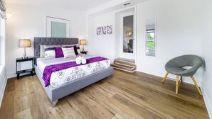 A modern bedroom with a large bed, a bedside table, a chair, and a view of the outside.