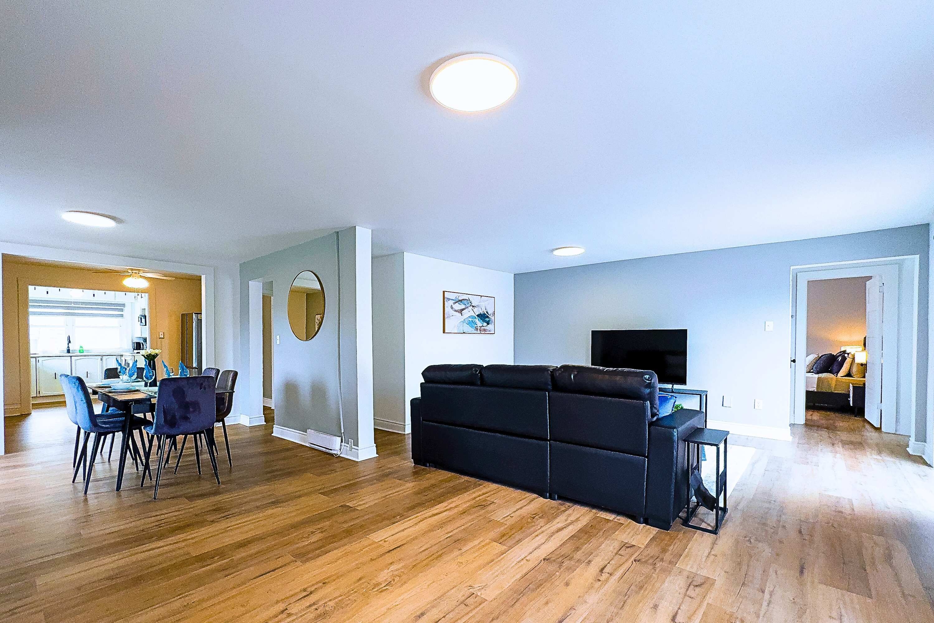Ein modernes Wohnzimmer mit einem schwarzen Sofa, Holzböden und einem Flachbildfernseher.