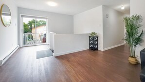 Une pièce spacieuse dotée d’un plancher en bois, d’une porte-fenêtre coulissante donnant sur un espace extérieur, d’une petite console noire et d’une plante en pot.