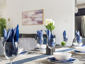 Een eetruimte met een tafel gedekt voor vier personen, met blauwe servetten, witte borden en heldere wijnglazen.
