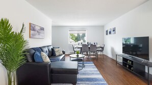 Un salon moderne avec un canapé, une table basse et un téléviseur. Il y a également un coin repas avec des chaises et une table.