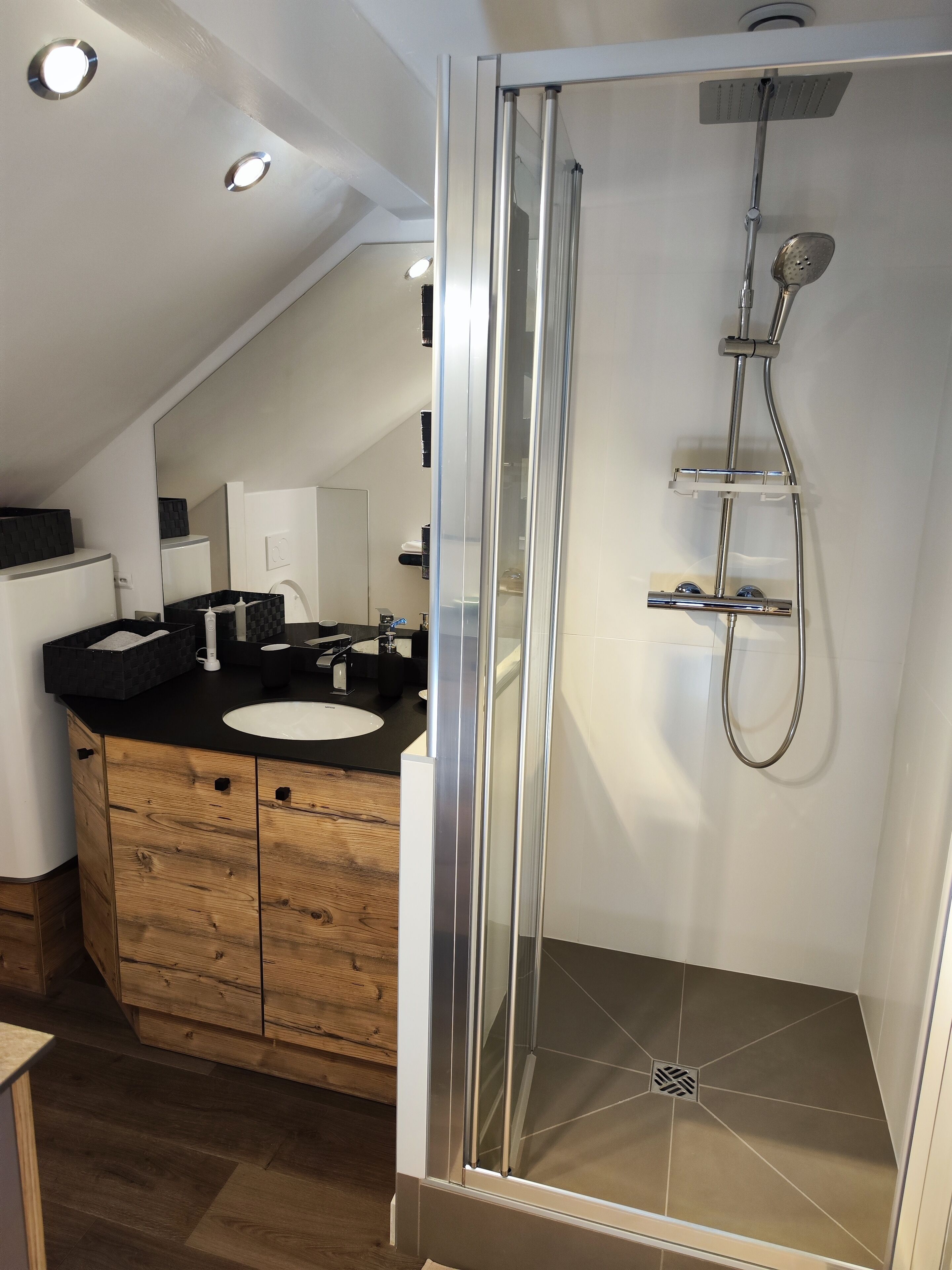 Un baño moderno con ducha envuelta en vidrio, tocador de madera con lavamanos y un espejo.