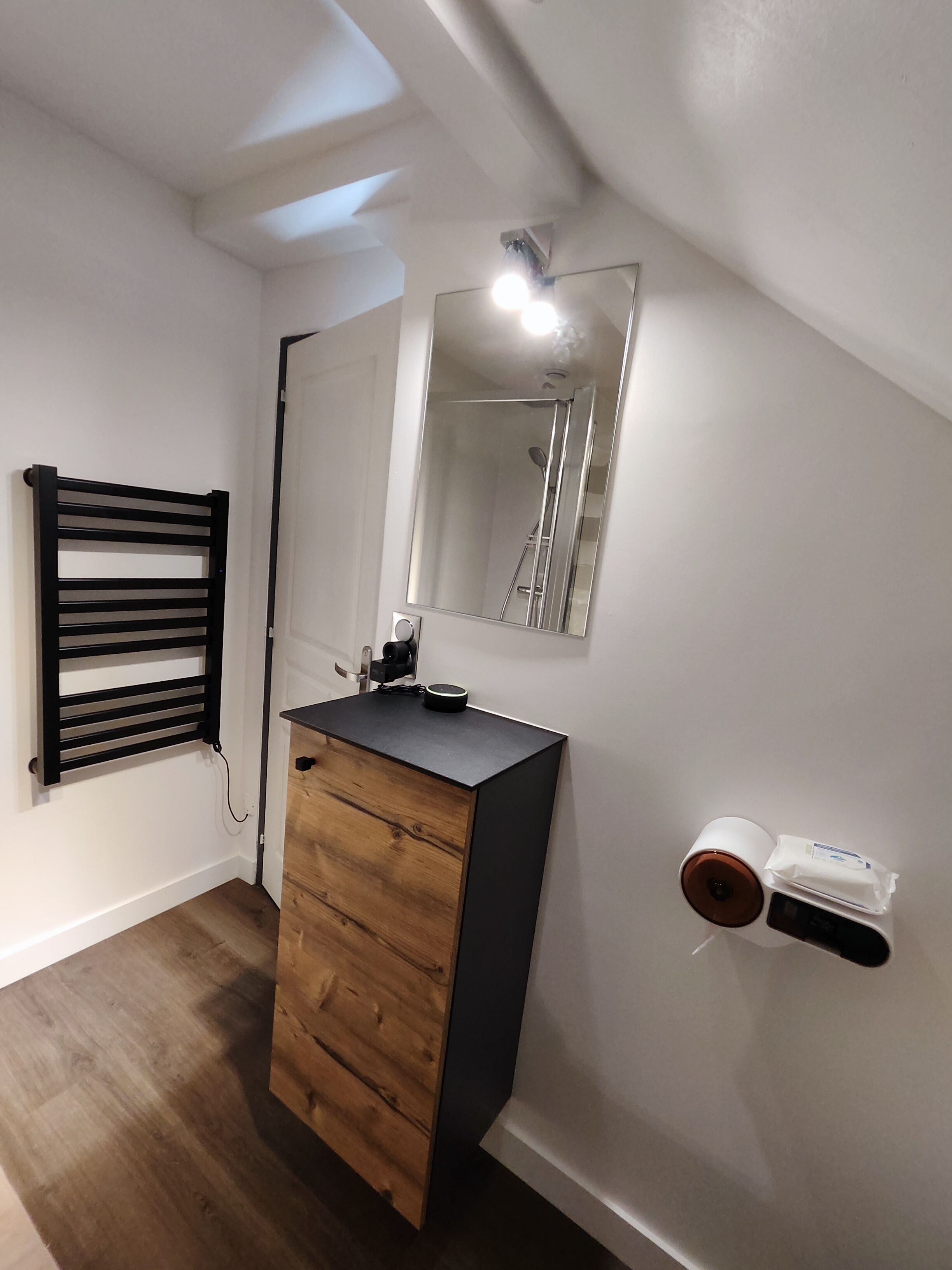 A modern bathroom with a wooden vanity, a black towel rack, a mirror, and a toilet paper holder.