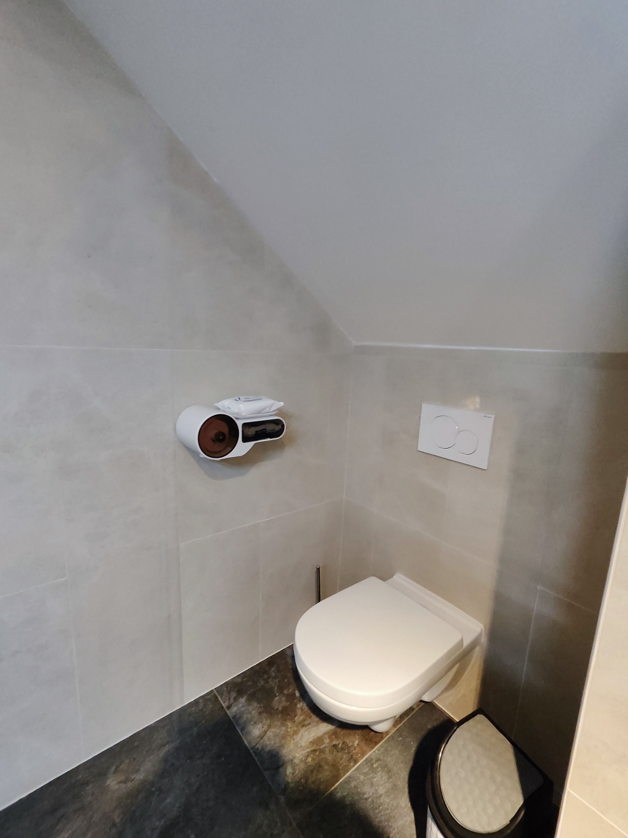 A small bathroom with a toilet, a towel dispenser, and a hand dryer mounted on the wall.
