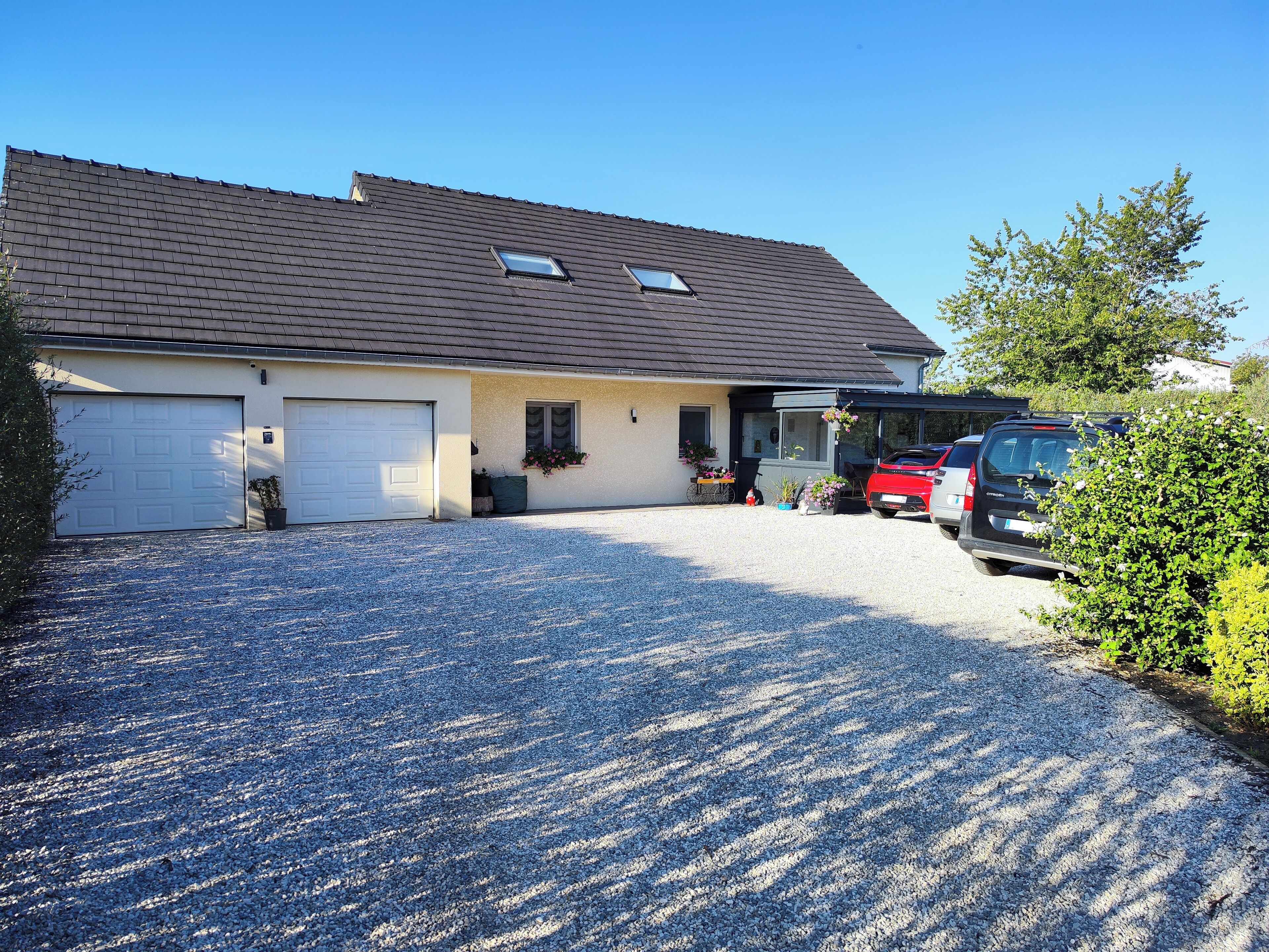 A two-story house with a gravel driveway, two garage doors, and a red car parked in the driveway.