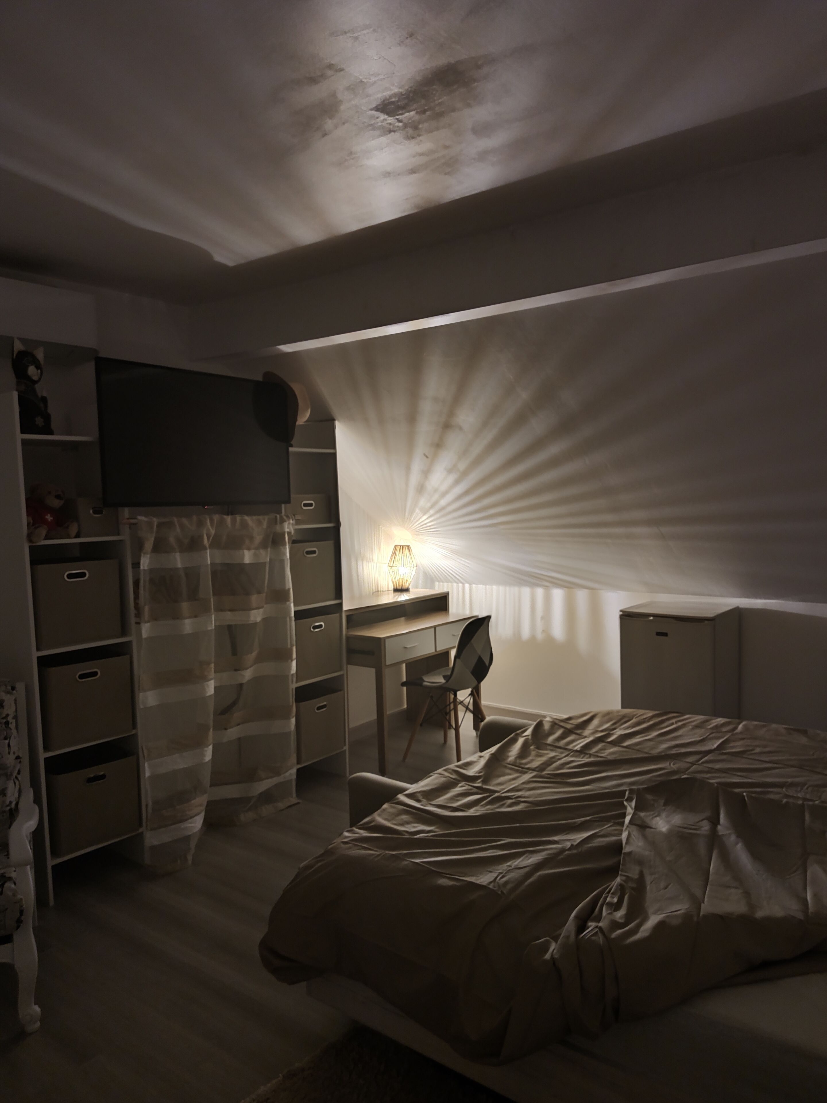 Une chambre à coucher faiblement éclairée, avec un lit, un bureau et une chaise.