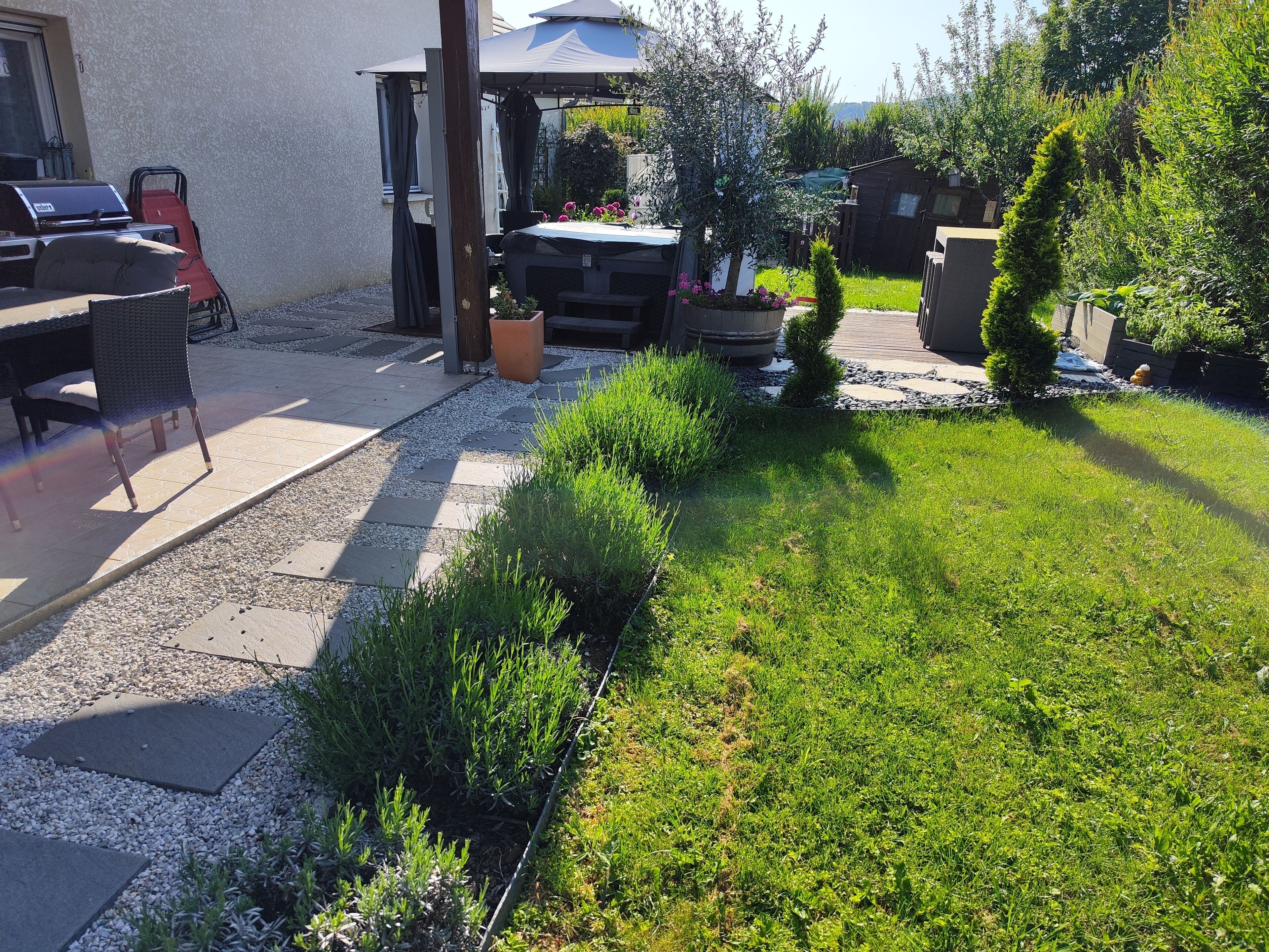 A patio area with outdoor furniture, a barbecue grill, and a garden with various plants and a small water feature.