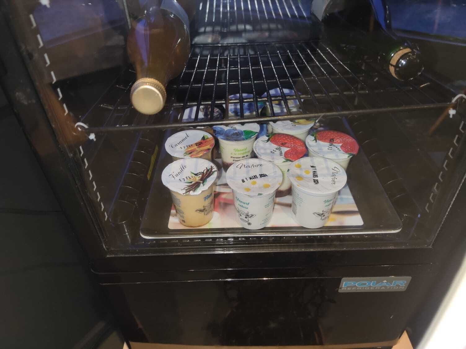 Un refrigerador con puerta de vidrio, que contiene varios yogures y una botella.