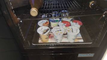 Un refrigerador con puerta de vidrio, que contiene varios yogures y una botella.