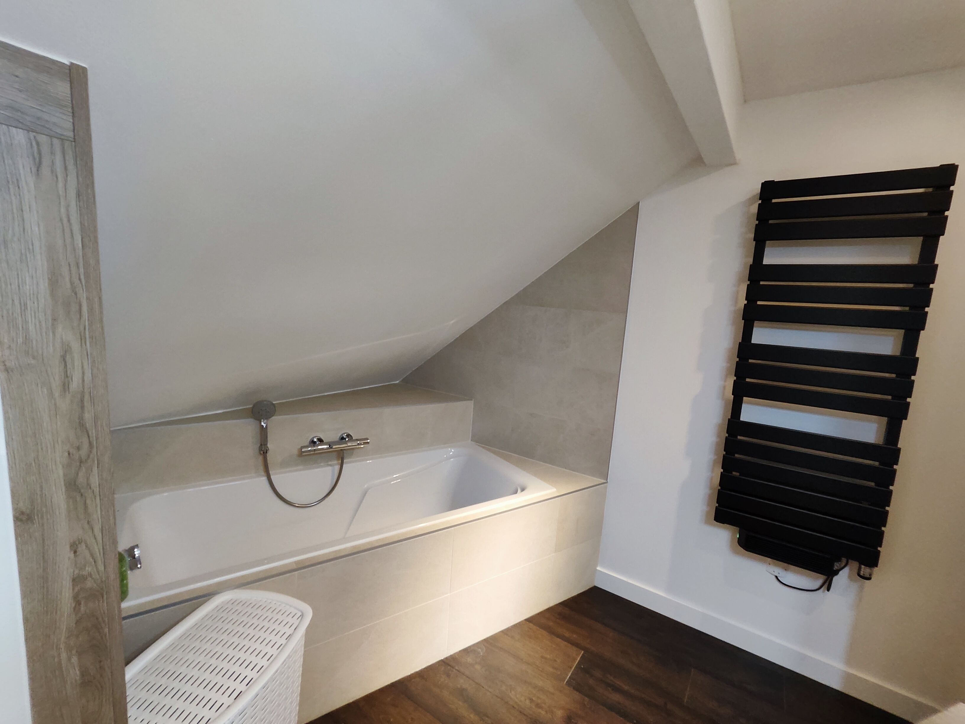 A bathroom with a bathtub, a white laundry basket, and a black towel rack.
