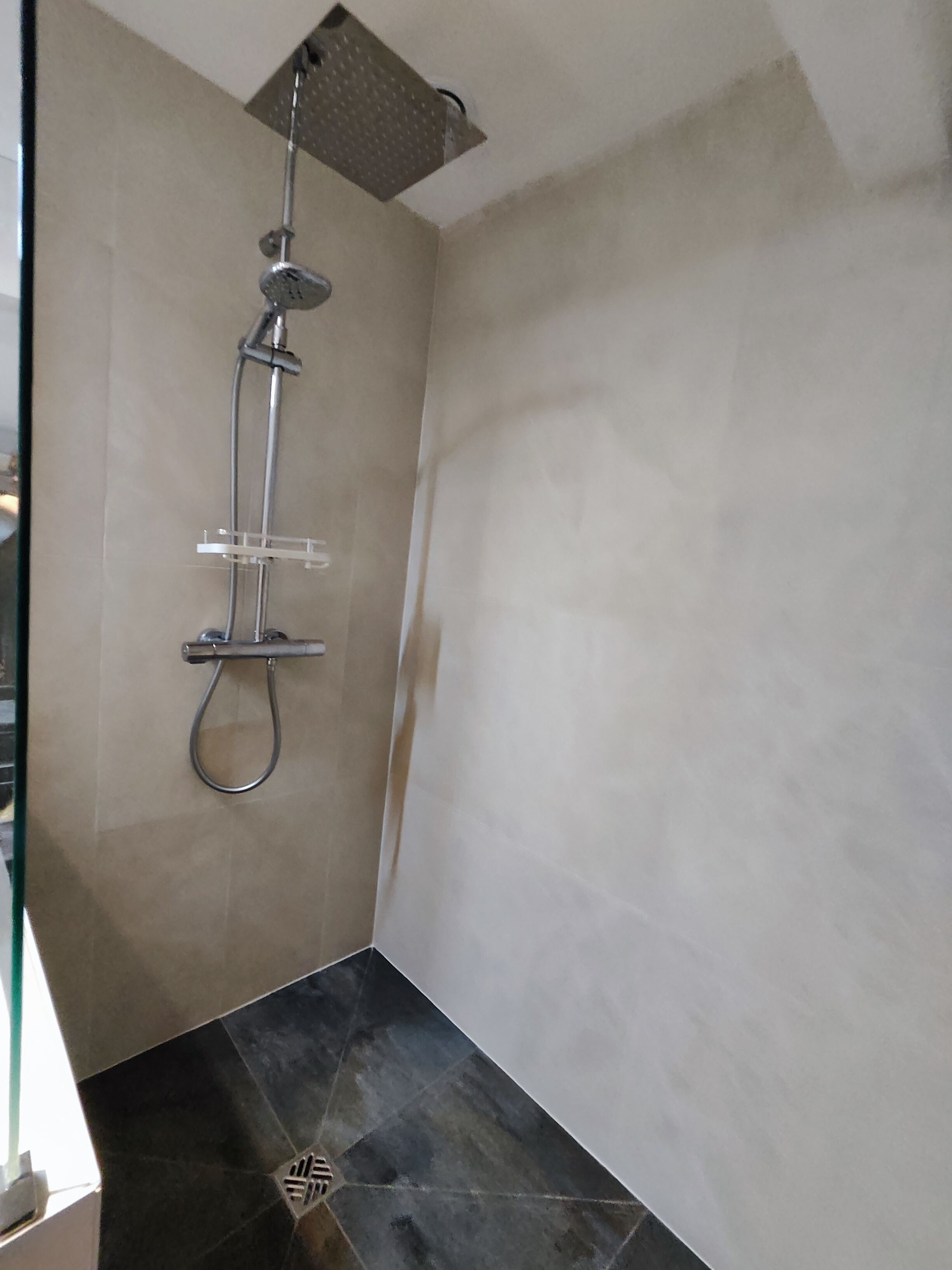 A shower with a handheld showerhead and a wall-mounted faucet.