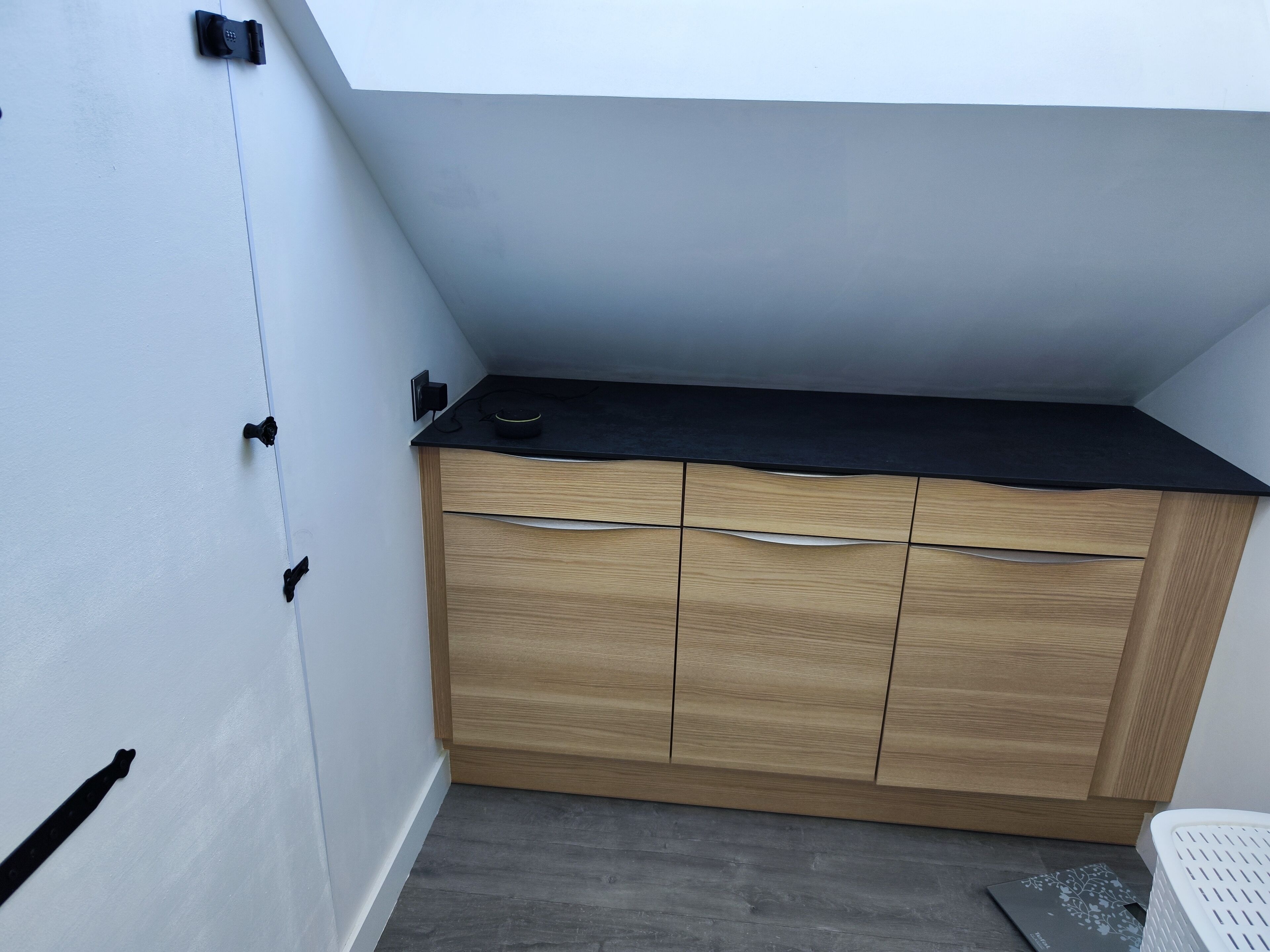 A compact kitchen with a black countertop, wooden cabinets, and a grey floor.