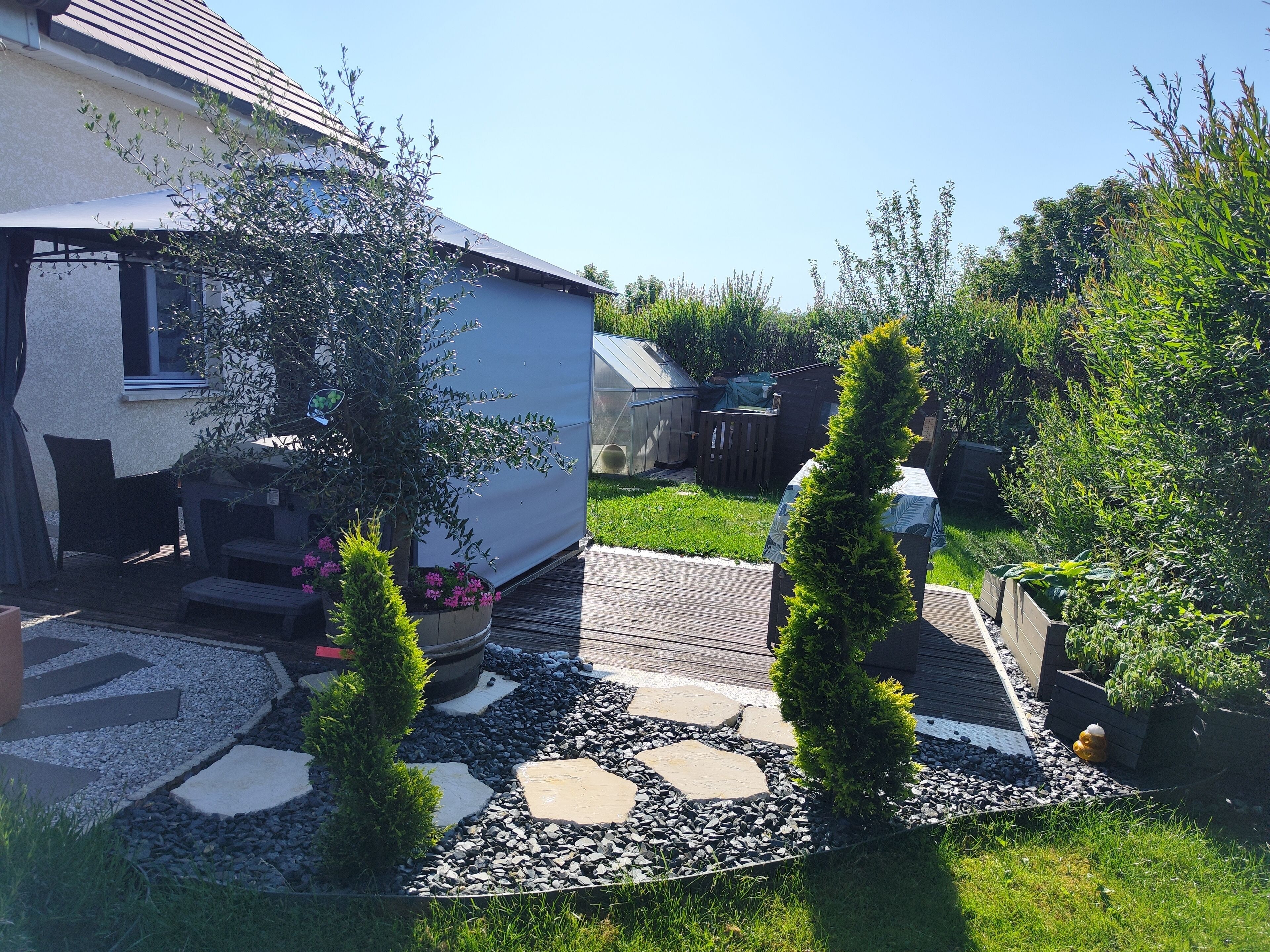 A house with a covered patio, a garden with a stone pathway, and a small shed in the background.