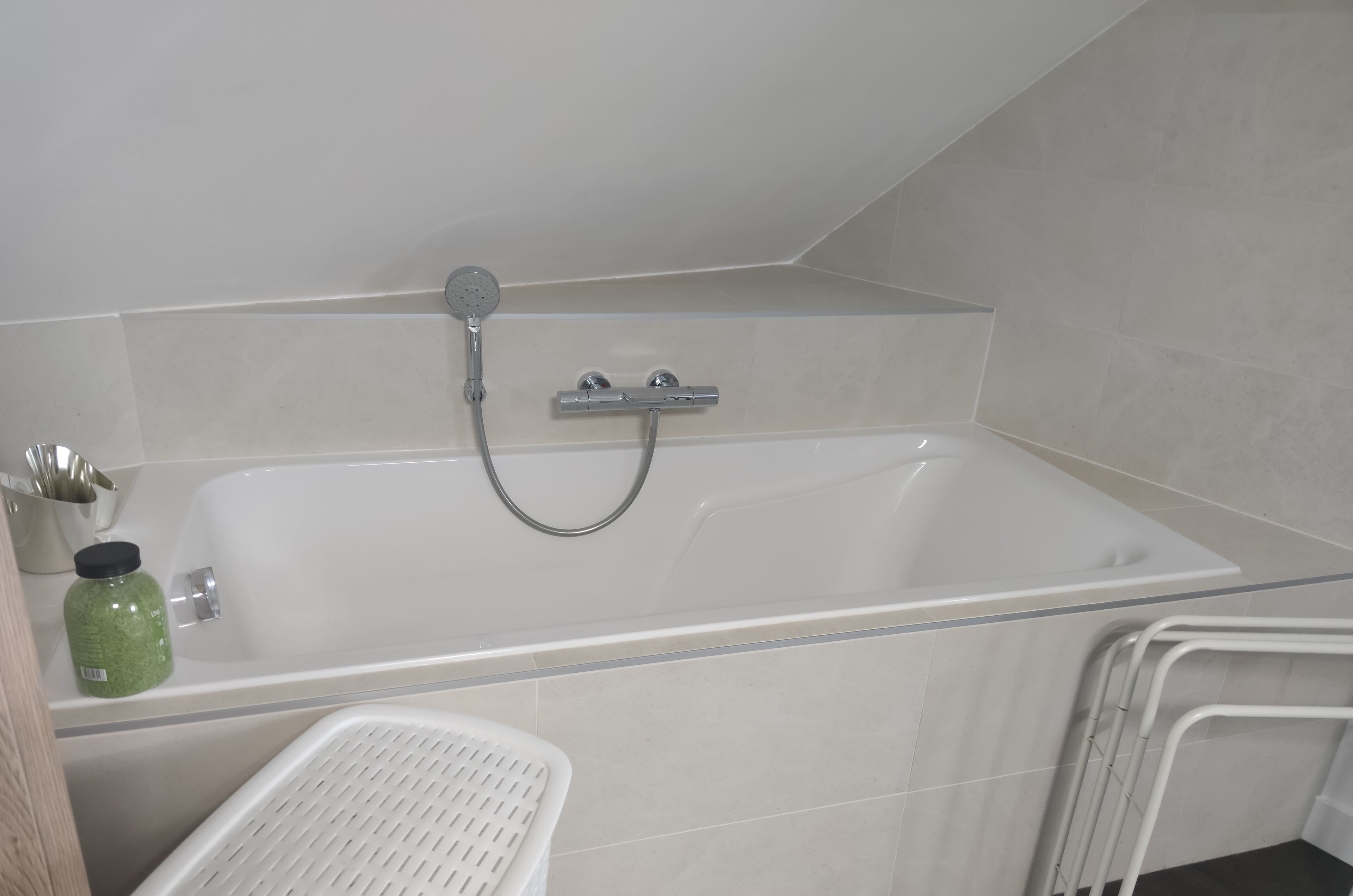 A modern bathroom with a white bathtub, a showerhead, and a small shelf with toiletries.